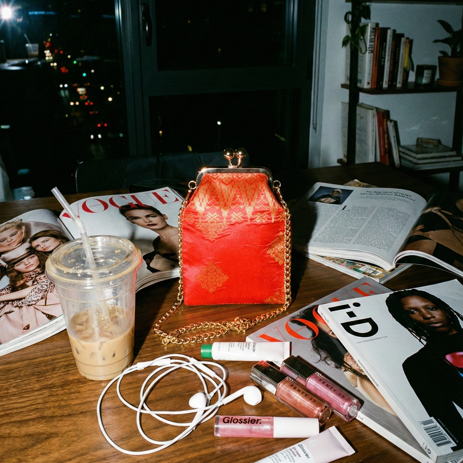 Red handbag on a table with magazines, a cup, and lip products.