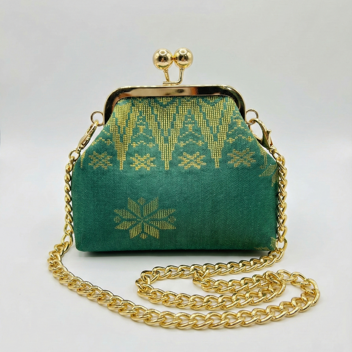 Green handbag with gold chain and intricate design on a white background